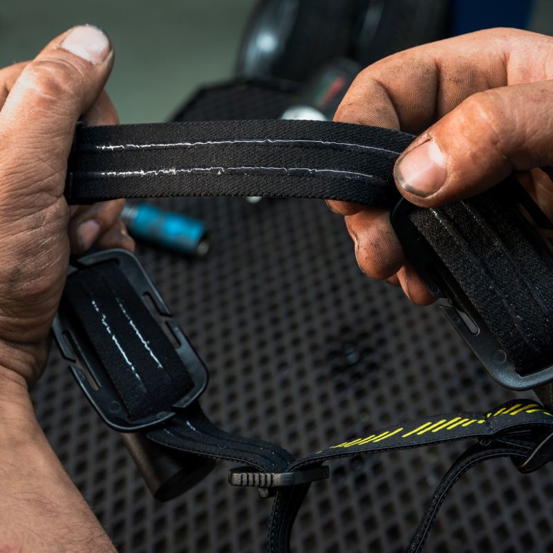 Close-up of a person's hands stretching a black adjustable headband with white stitching, showing its elastic material and buckle.