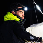 A man wearing a Ledlenser H19R headlamp and a bright neon yellow hood over a black jacket, photographed in a dark setting with dramatic lighting.