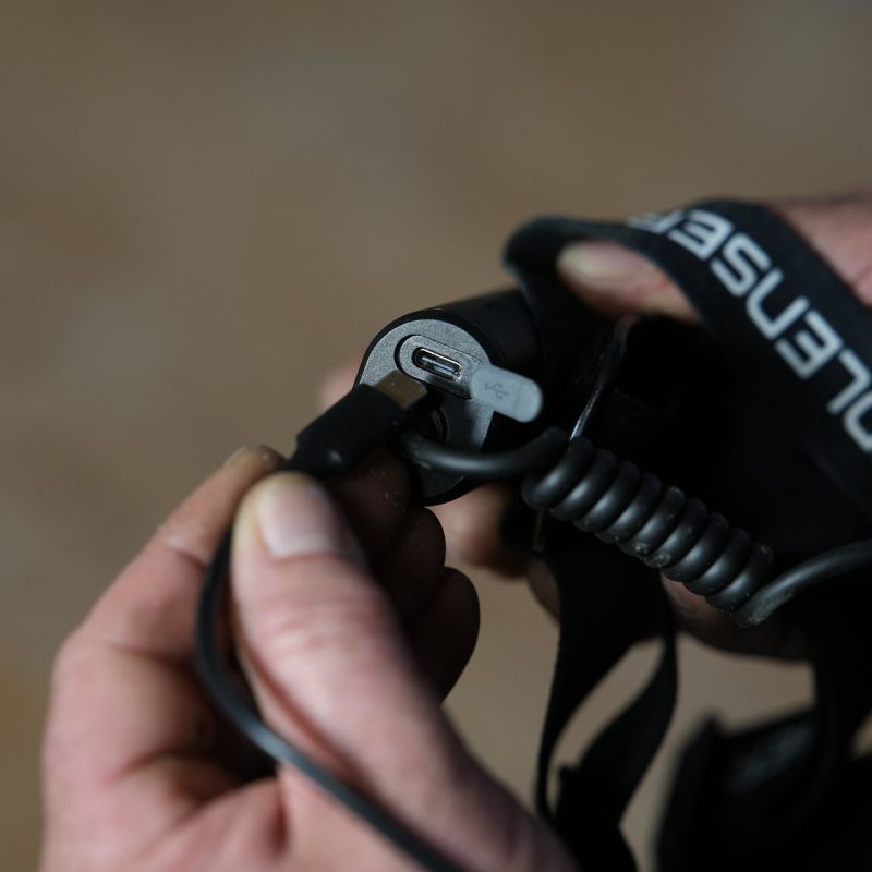 Close up of person plugging a charger into the battery pack of a Ledlenser headlamp.