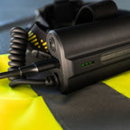 A close-up of a black Ledlenser H149R Pro headlamp battery with a coiled cable, resting on a high-visibility yellow and black safety vest.