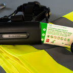 A close-up of a black Ledlenser H19R Pro headlamp battery pack with a white and green product label, resting on a bright yellow high-visibility fabric surface.