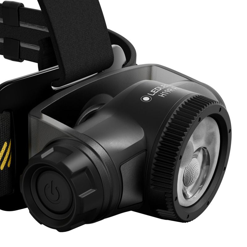 A close-up studio shot of a black Ledlenser H19R Pro headlamp with a textured front lens, power button, and part of the adjustable head strap on a white background.