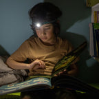 Young boy wearing a Ledlenser KIDLED4R headlamp to read a book after lights light - Dinosaurs Pattern