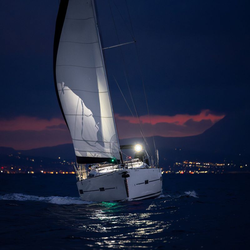 Boat under sale at night. It has a white hull and white sails and is leaning to the starboard side