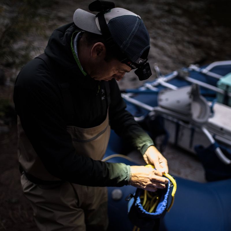 Person preparing a boat with a yellow rope, wearing a Ledlenser H19R Core headlamp, cap and dark jacket.