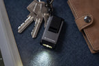 Ledlenser K4R rechargeable Keyring Light switched on and sitting next to pocket book and set of keys - Black