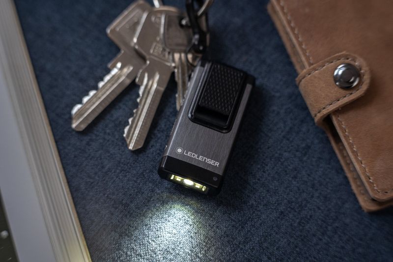 Ledlenser K4R rechargeable Keyring Light switched on and sitting next to pocket book and set of keys - Black